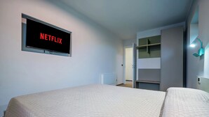 A hotel room with a bed, a wall-mounted TV displaying 'NETFLIX,' a wardrobe, and a small bedside table. - Casa Matilla - Blu - One Bedroom Apartment, Sleeps 4 (La Morra)