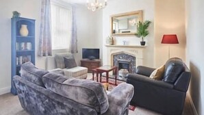 Ein Wohnzimmer mit Kamin, einem blauen Bücherregal, einem grauen Sofa und einem schwarzen Sessel.