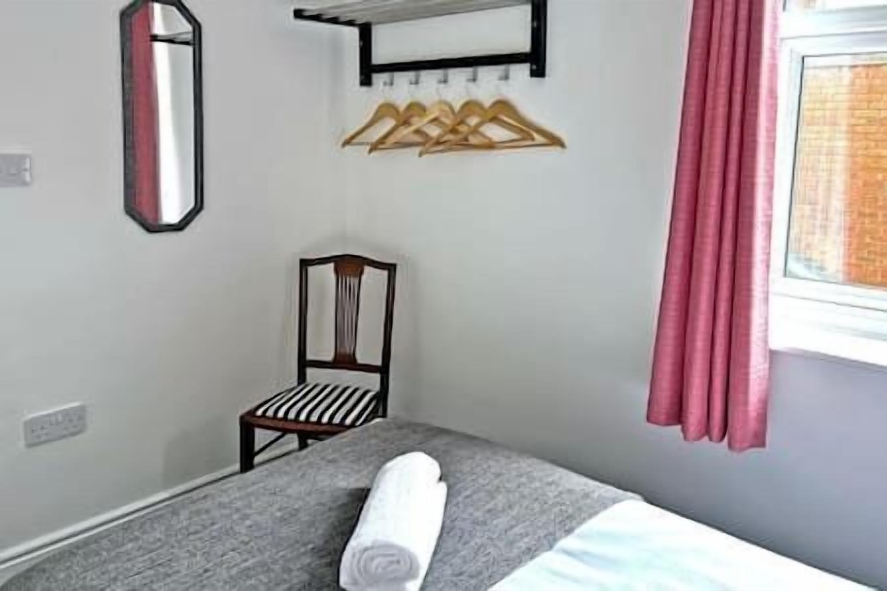 A bedroom with a bed, a chair, a mirror, and a window with curtains.