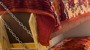 Ένα κρεβάτι με δύο κουκέτες, με μια κόκκινη κουβέρτα και ένα σεντόνι με σχέδια λουλουδιών.