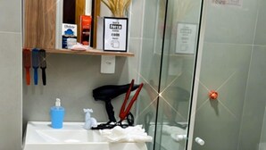 Ένα σύγχρονο μπάνιο με ένα διαχωριστικό ντους από γυαλί, έναν ξύλινο νιπτήρα και ένα μικρό φυτό σε γλάστρα.