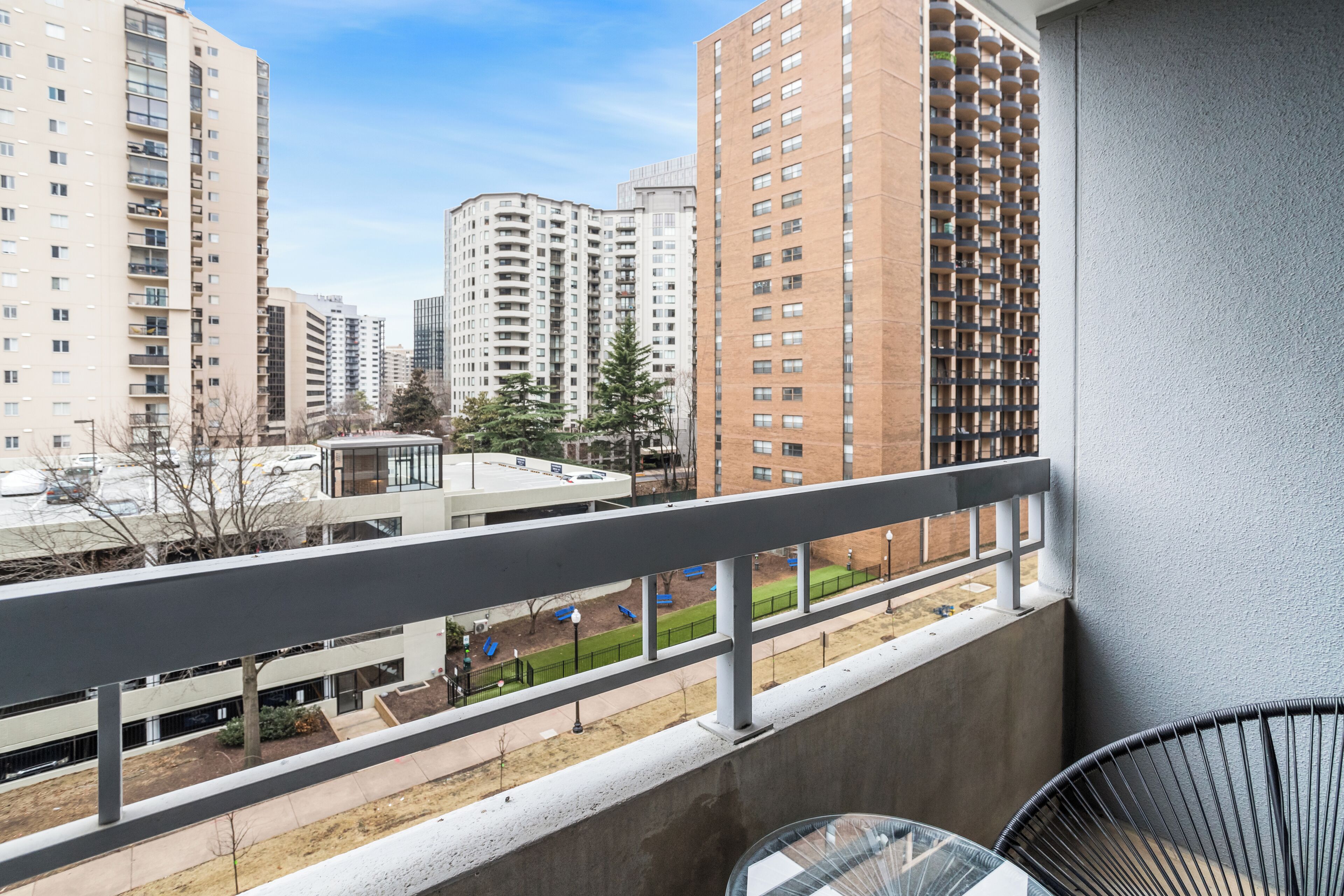 A balcony with a view of high-rise buildings, a clear sky, and a parking area.