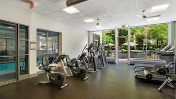 Un gimnasio con cintas de correr, elípticas y equipo de pesas. Hay una puerta de vidrio que da a una zona de piscina.