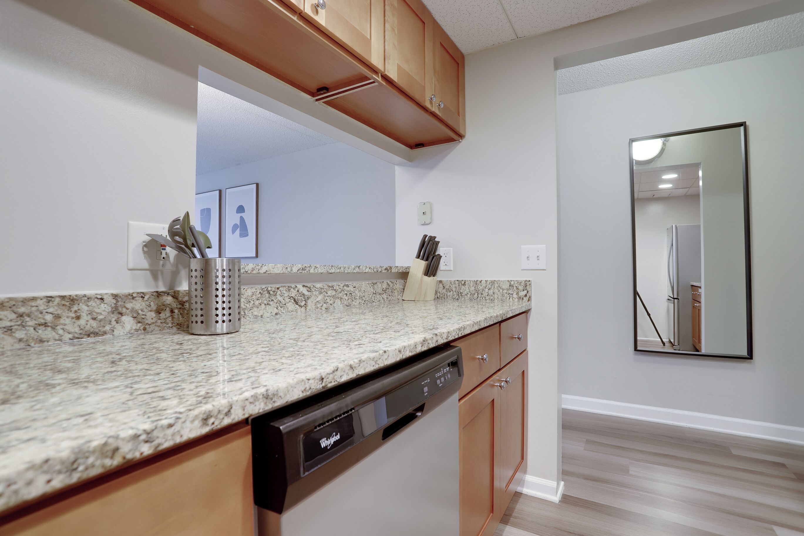 A kitchen with granite countertops, wooden cabinets, a dishwasher, and a mirror on the wall.