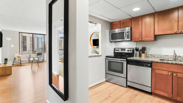 A modern kitchen with stainless steel appliances, wooden cabinets, and a granite countertop. - Crystal City Apartments near Reagan Airport - We Host (Arlington)