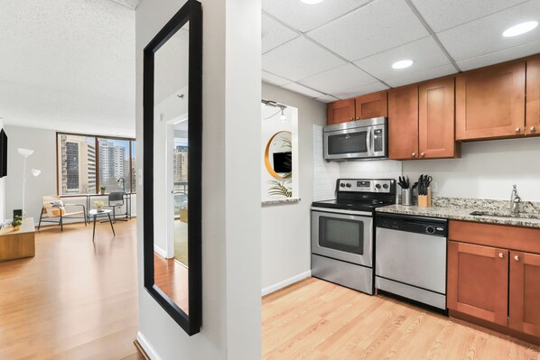 A modern kitchen with stainless steel appliances, wooden cabinets, and a granite countertop. - Crystal City Apartments near Reagan Airport - We Host (Arlington)