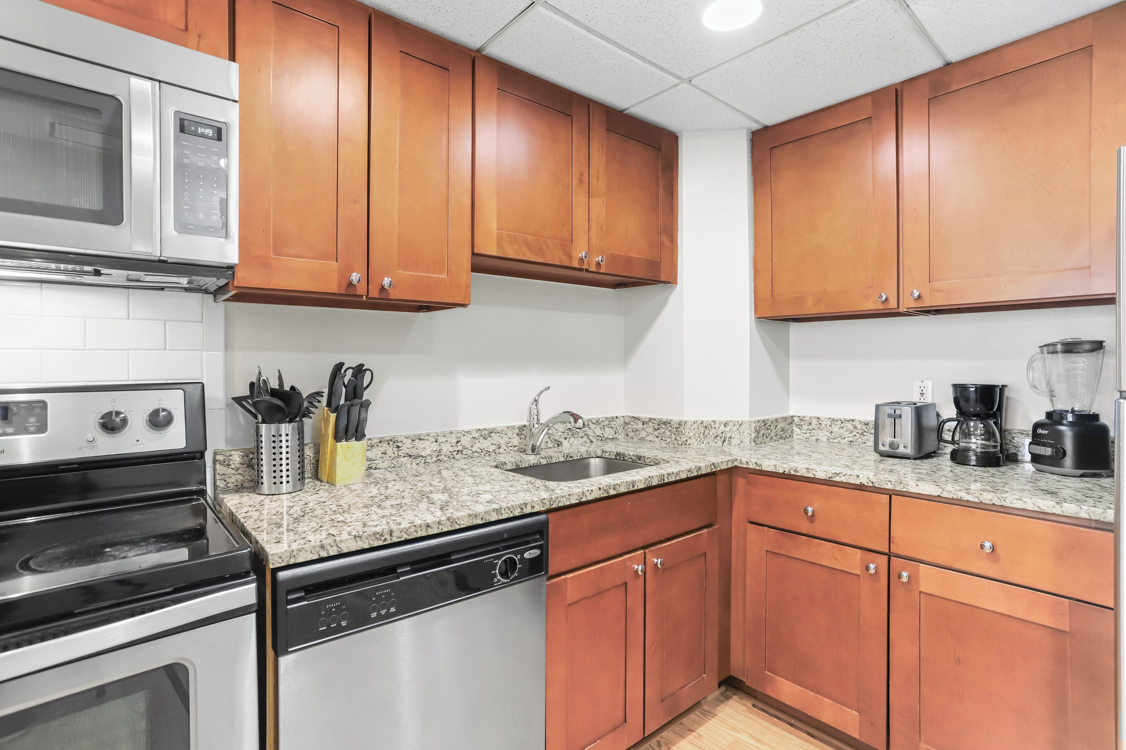 A kitchen with wooden cabinets, a granite countertop, a microwave, a dishwasher, a sink, and a coffee maker.