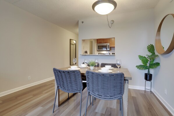 A dining area with a wooden table, two grey wicker chairs, and a potted plant. - Crystal City Apartments near Reagan Airport - We Host (Arlington)