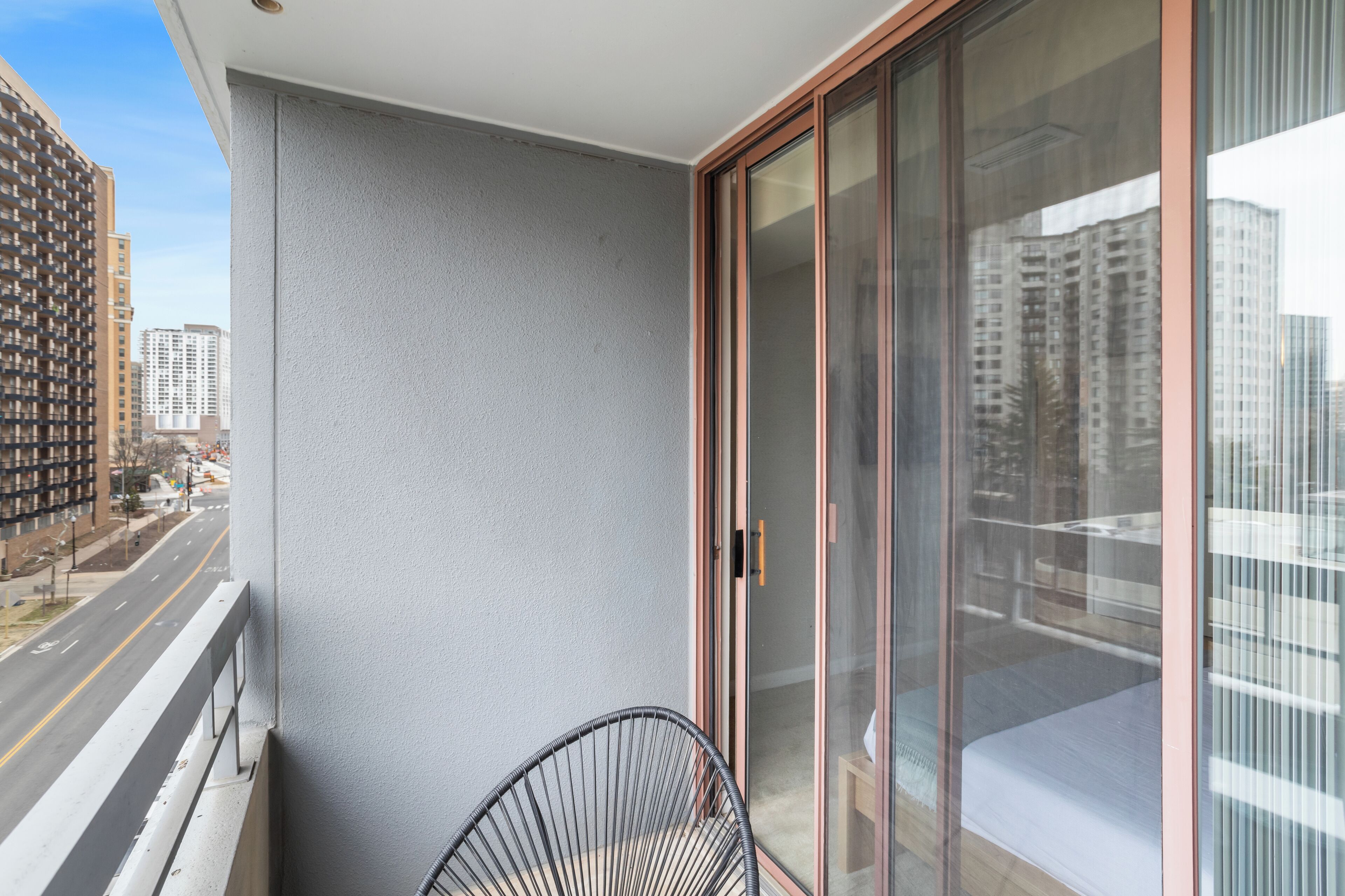 A balcony with a chair, a sliding glass door, and a view of a city street.