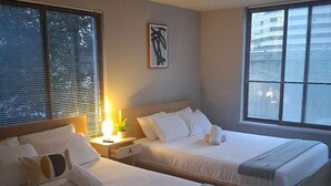 A hotel room with two beds, a bedside table with a lamp, a window with blinds, and a framed picture on the wall. - Crystal City Apartments near Reagan Airport - We Host (Arlington)