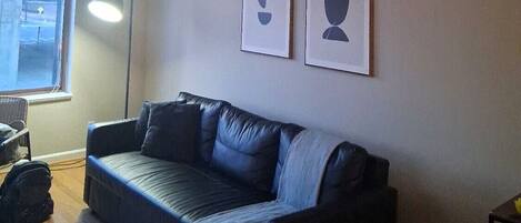 A living room with a black leather sofa, a standing lamp, and two framed abstract art pieces on the wall.