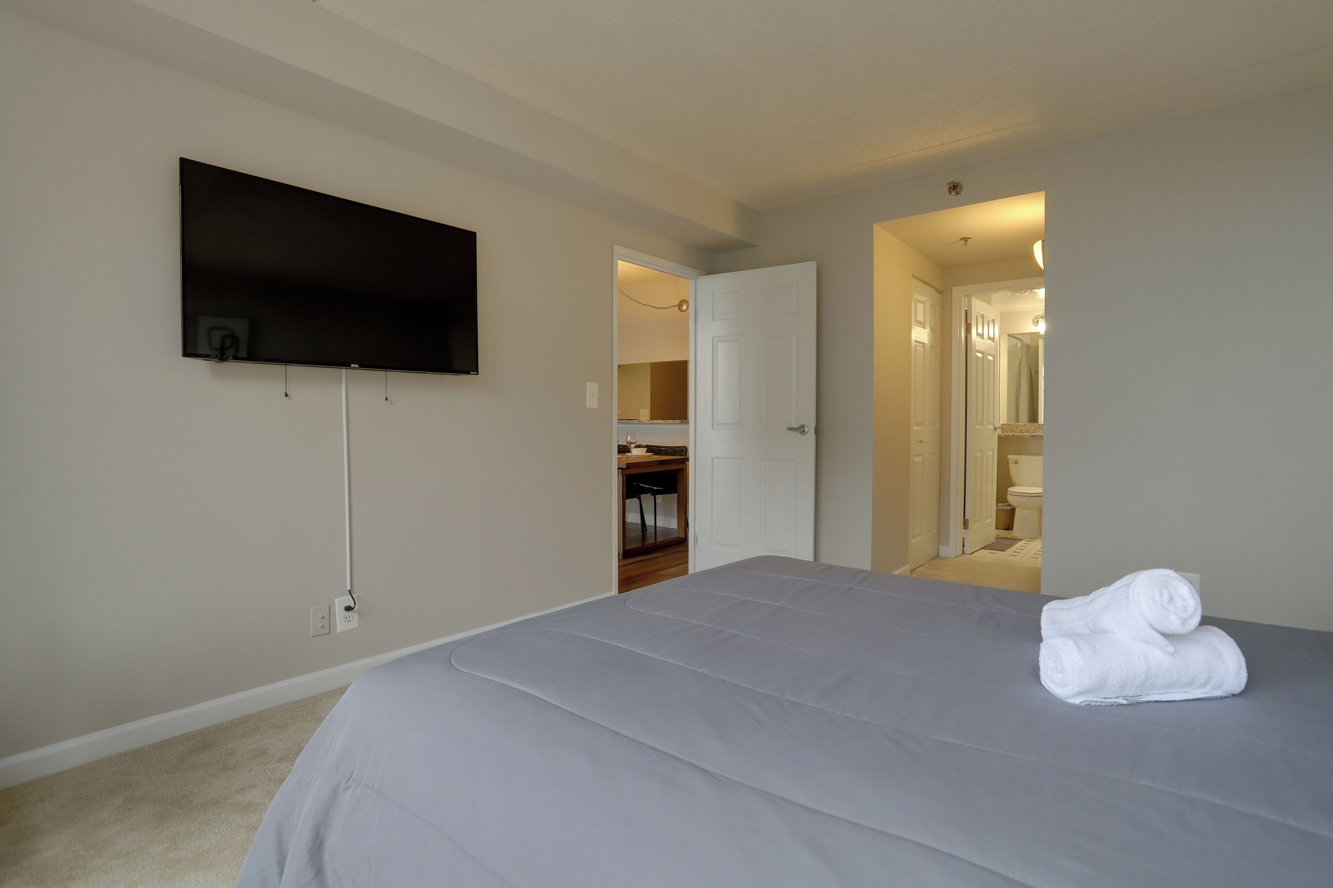 Ein Schlafzimmer mit einem Bett, einem flachbildfernseher an der Wand und einem durch eine offene Tür einsehbaren Badezimmer.