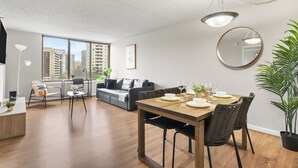 A modern living room with a dining area, large windows, and a city view.