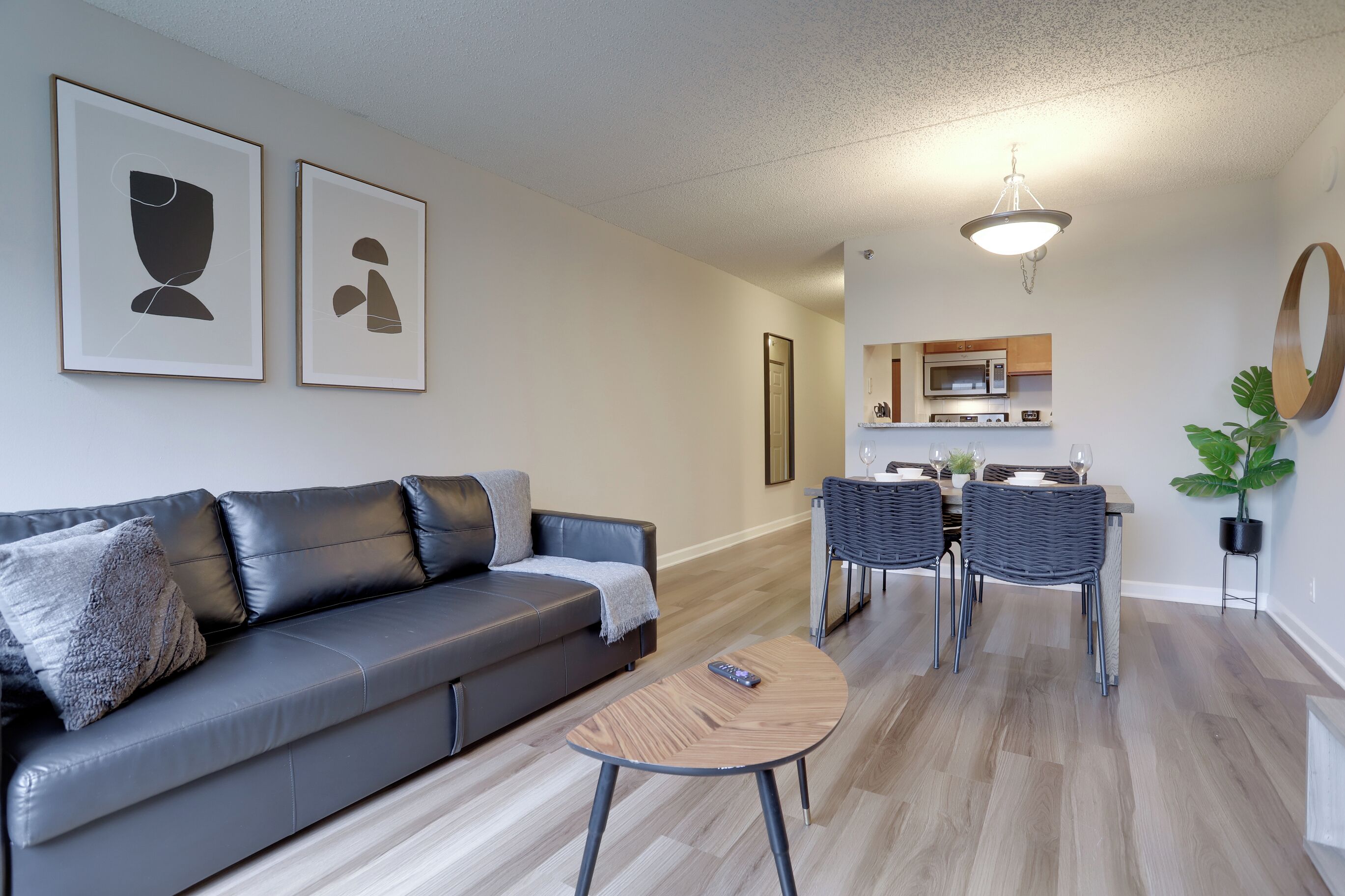A modern living room with a grey leather sofa, a round wooden coffee table, and a dining area with two wicker chairs and a small table.