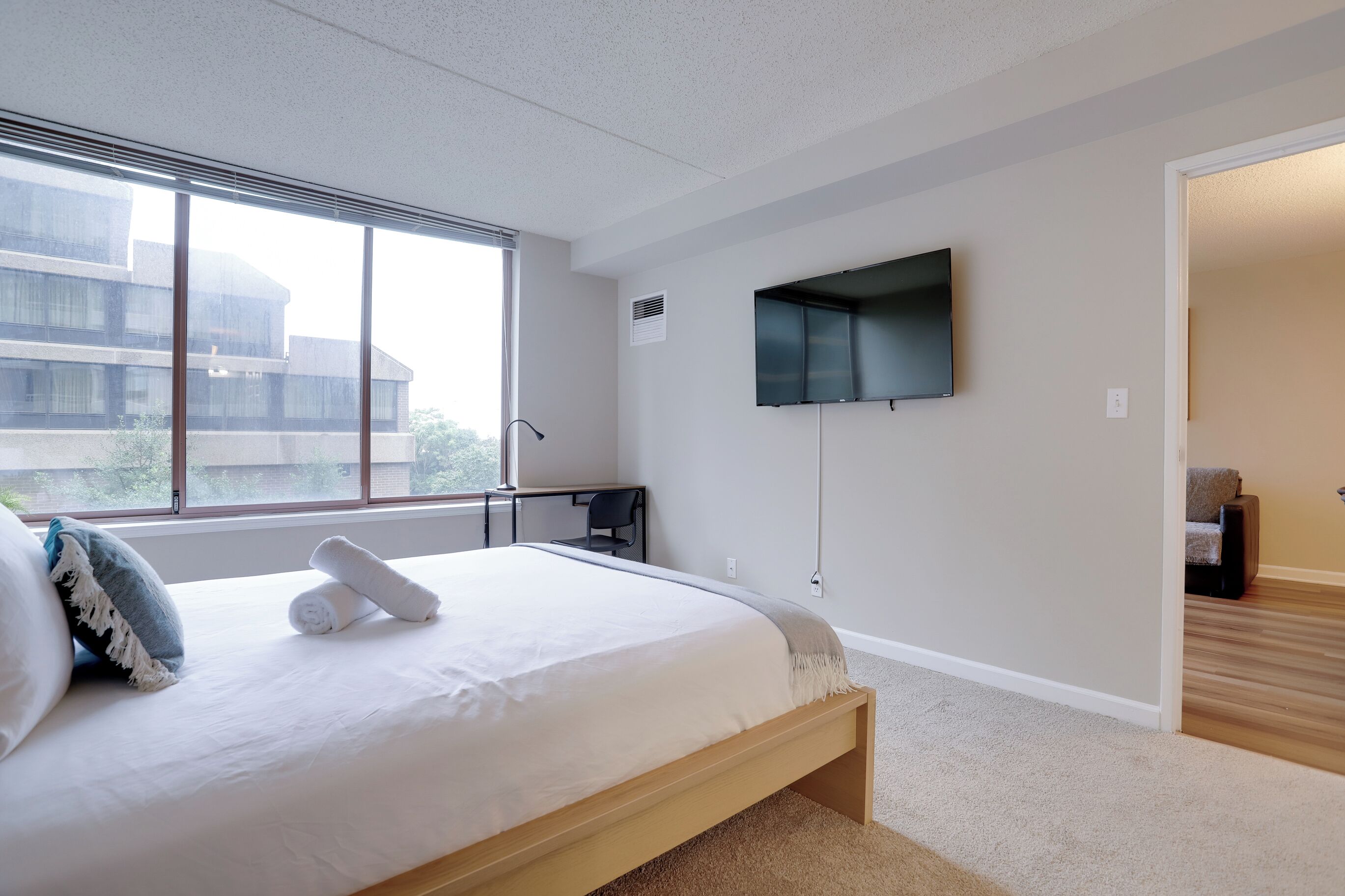 Une chambre moderne avec un grand lit, un téléviseur fixé au mur et une vue sur un bâtiment à l’extérieur.