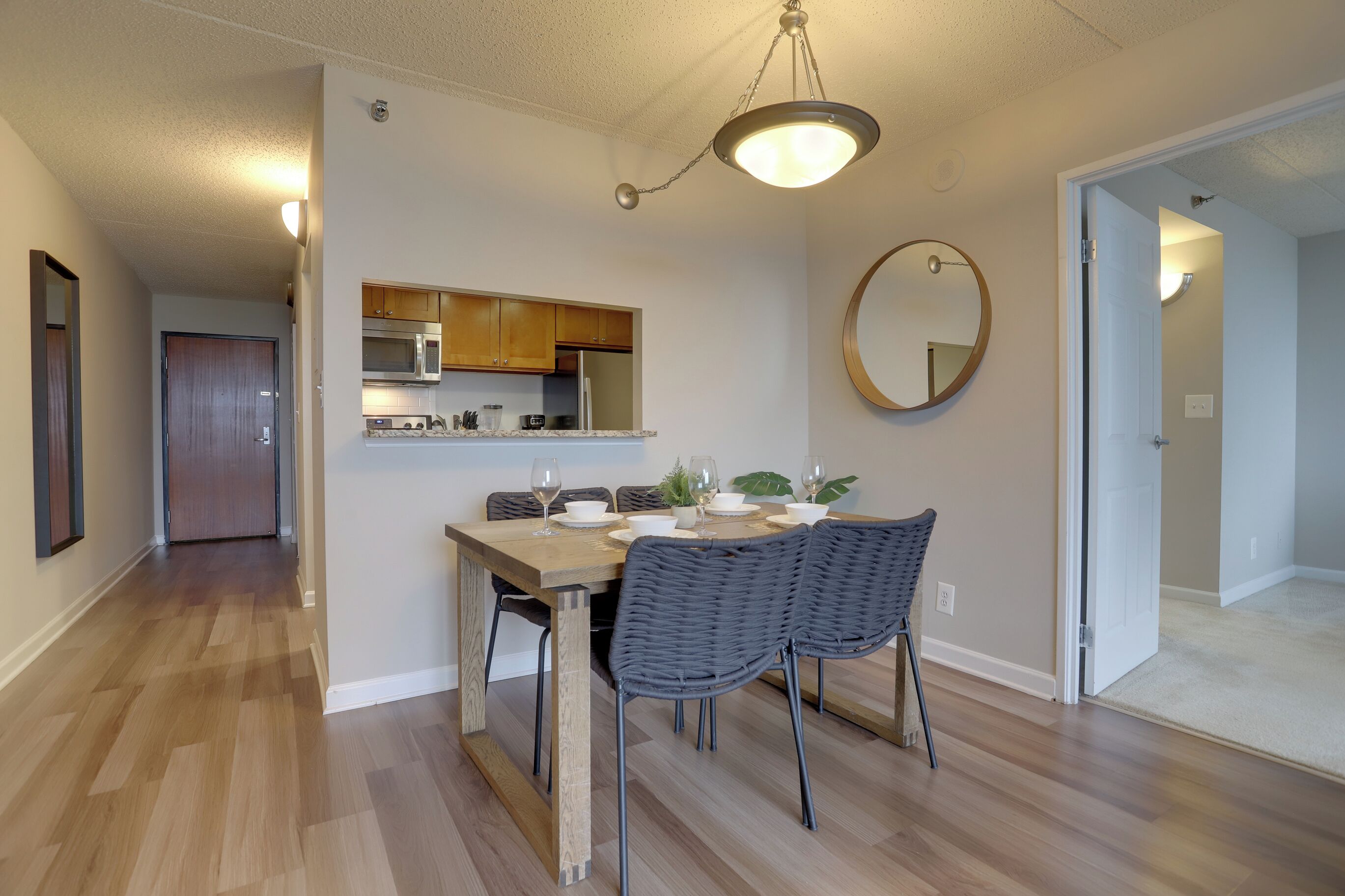 A modern kitchen with wooden cabinets, a microwave, and a dining area with a wooden table and two chairs.