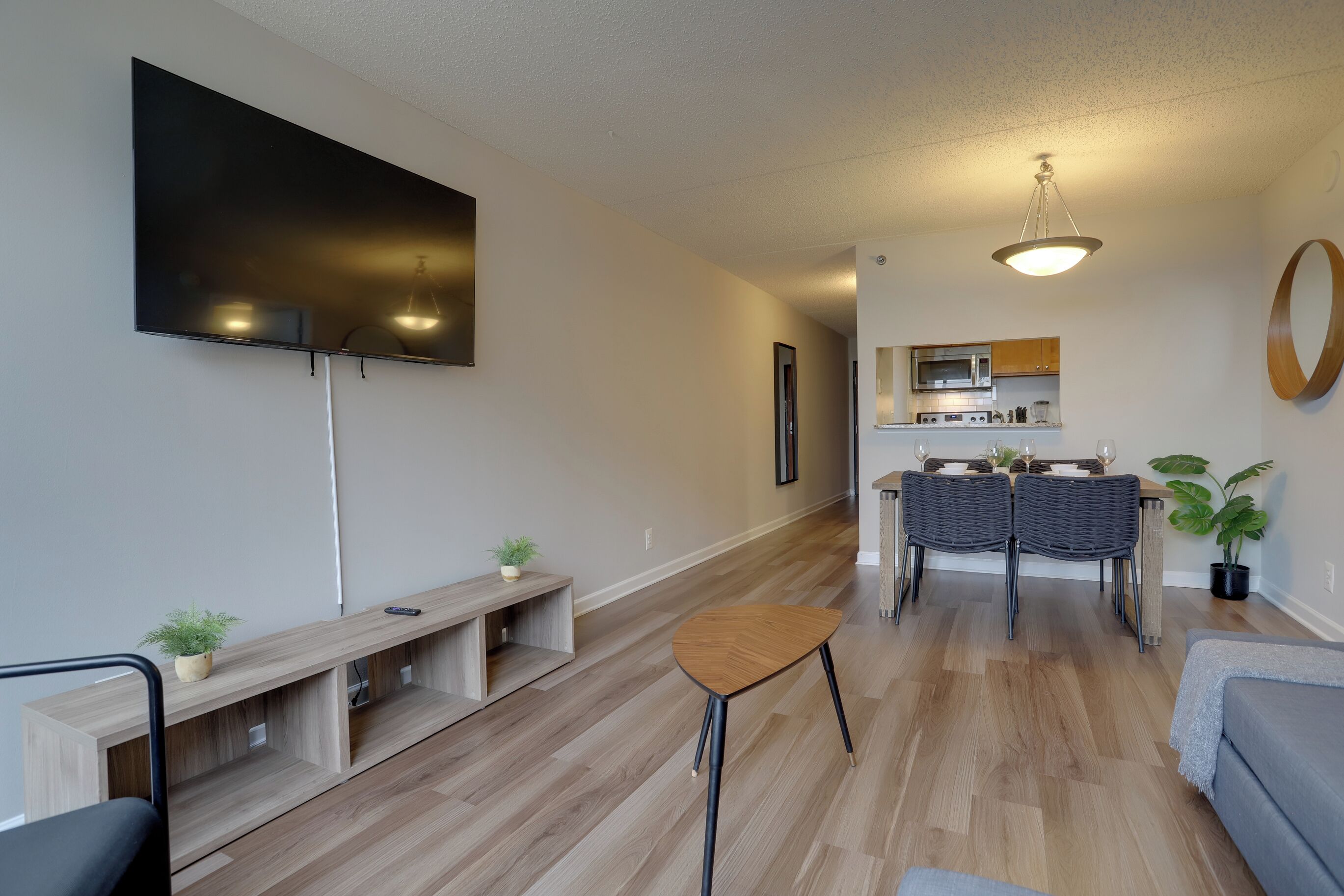 A modern living room with a flat-screen TV, a dining area with a table and chairs, and a kitchen in the background.