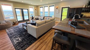 A spacious living room with a large sofa, a dining area with a wooden table, and a kitchen with a sink and refrigerator.