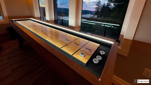 A pool table with a view of a lake and mountains through large windows.
