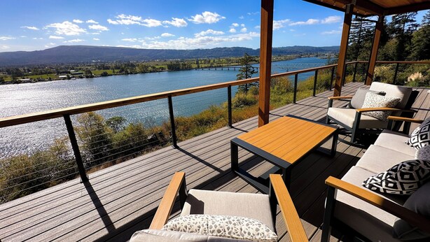 A deck with outdoor furniture overlooking a river and mountains.