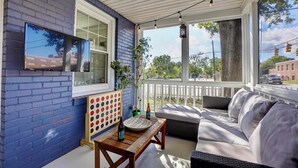 A covered porch with a blue brick wall, a wooden table with a board game, a sofa, and a TV mounted on the wall.