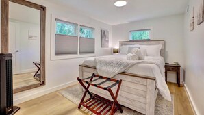 A bedroom with a bed, a wooden chair, a large mirror, and a heater.
