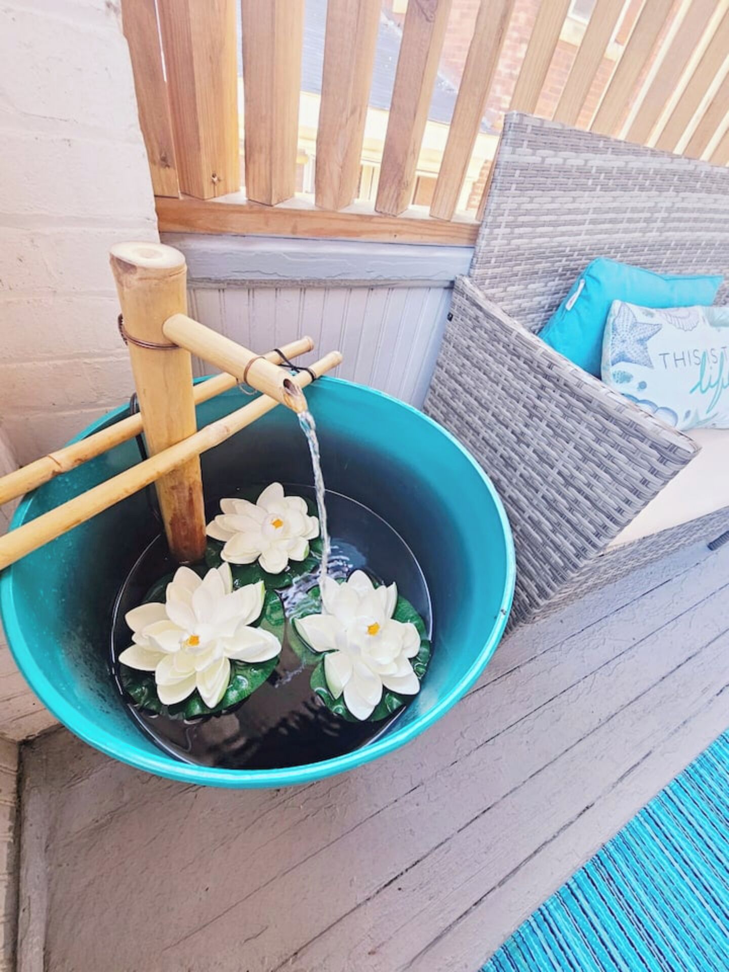 Ein Eimer mit Wasser und Lotusblumen, eine Holzkonstruktion sowie ein Korbstuhl mit Kissen.