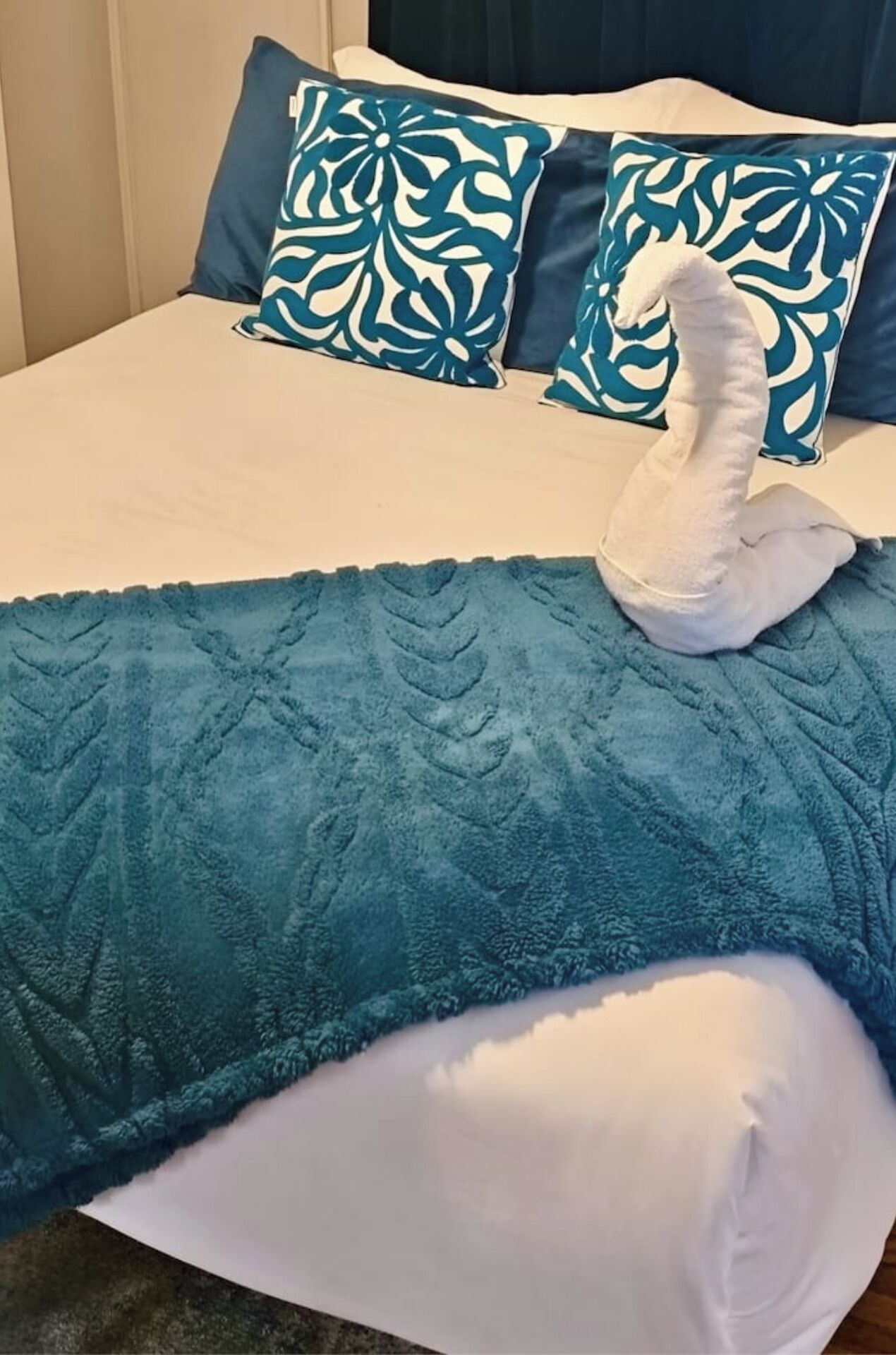 A bed with a teal blanket and a white swan-shaped pillow.