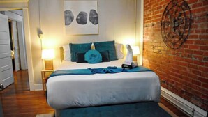 Une chambre à coucher avec un lit double, une literie de couleur turquoise, un mur en briques et un élément décoratif en métal.