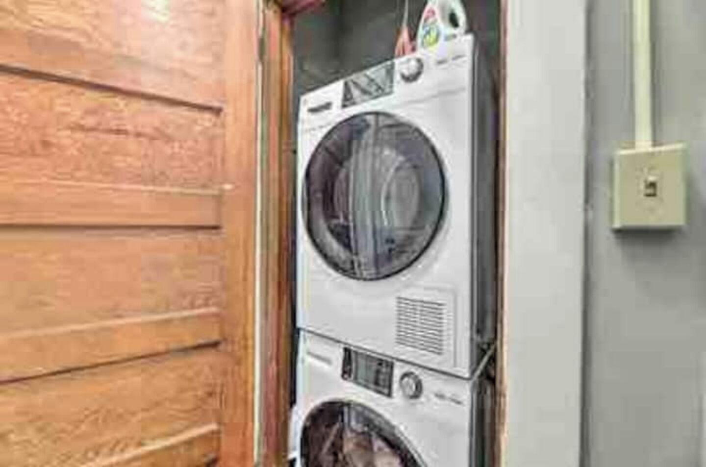 A stacked washer and dryer unit in a laundry room with a wooden door and a light switch on the wall.