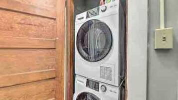 A stacked washer and dryer unit in a laundry room with a wooden door and a light switch on the wall.