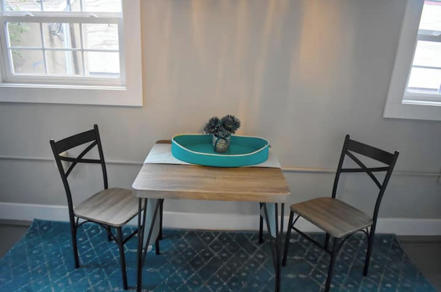 A small dining area with a table and two chairs, a teal bowl with decorative items, and a patterned rug.