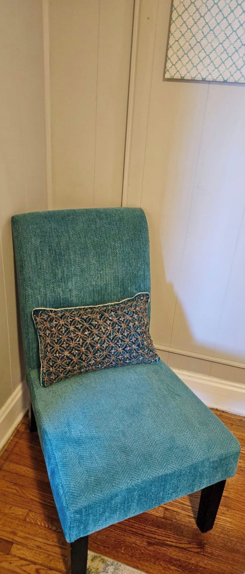 A teal armchair with a patterned pillow against a wall with a decorative panel.