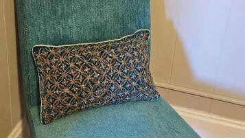 A teal armchair with a patterned pillow against a wall with a decorative panel.