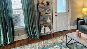 A living room with a wooden floor, a patterned rug, a bookshelf, a door, and a lamp. - Espresso Maker & Modern Decor by Arena, University, Hospitals (Huntington)