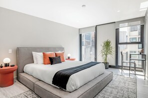 Ein modernes Schlafzimmer mit einem großen Bett, einer Topfpflanze und Blick auf die Stadt durch das Fenster.
