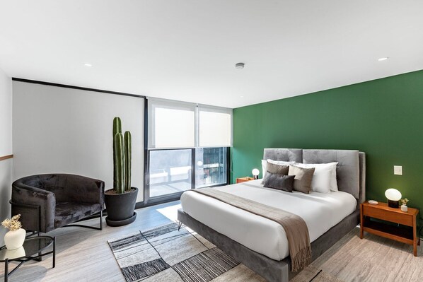 Ein modernes Schlafzimmer mit einem großen Bett, einem Sessel, einer Topfpflanze und Blick durch ein großes Fenster.