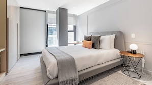 A modern bedroom with a large bed, a bedside table with a lamp, and a view of the city through a large window. - Blueground Mexico City JVM 429 (Mexico City)