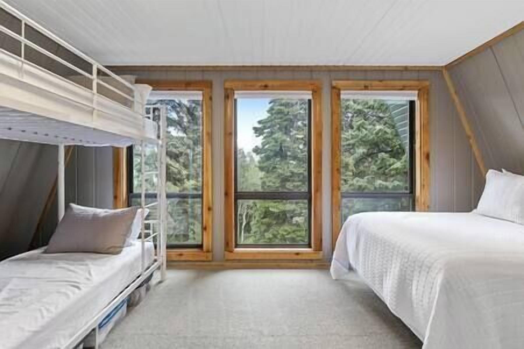 Una habitación con literas, ventanas amplias y vistas a árboles.