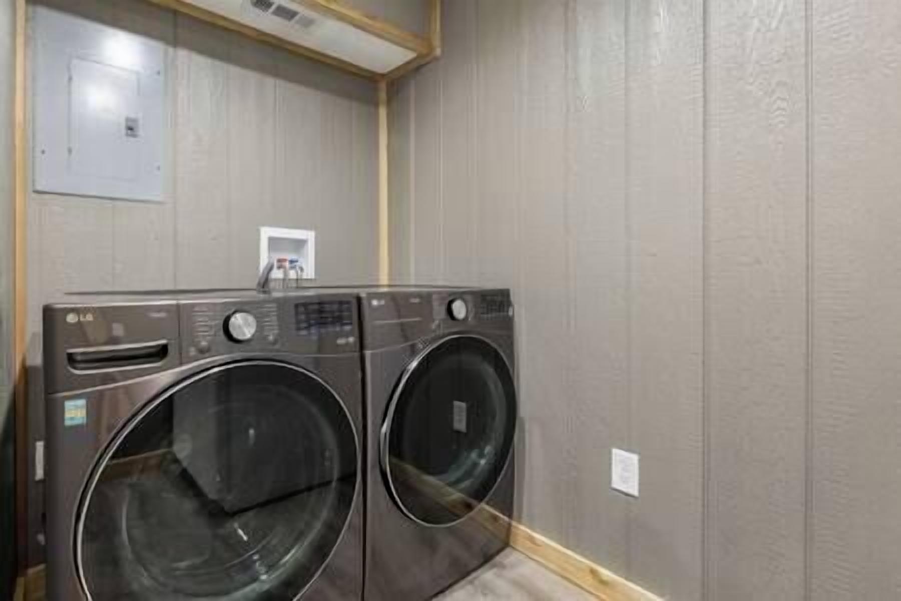 A laundry room with two front-loading washing machines and a small electrical outlet on the wall.