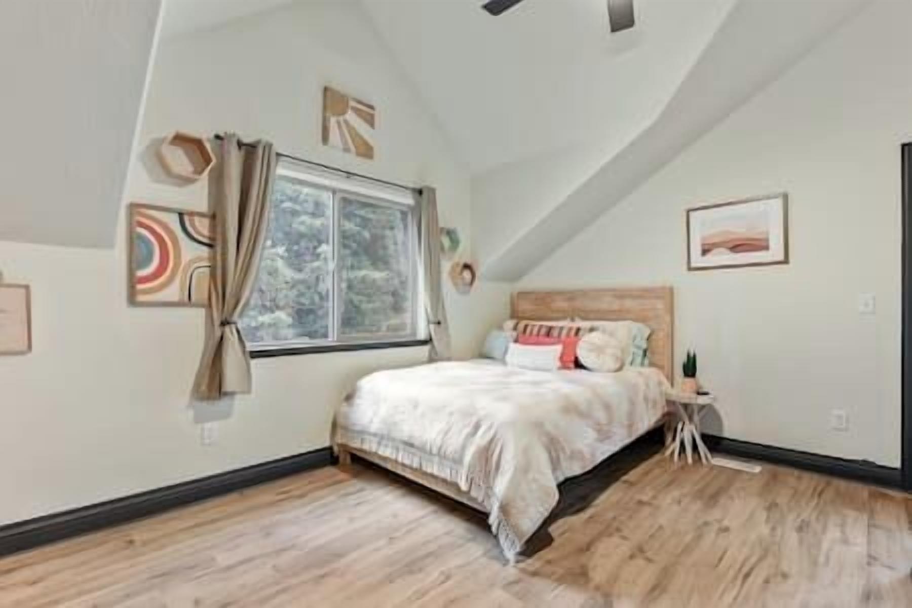 Ein Schlafzimmer mit großem Fenster, einem Bett mit weißer Bettwäsche und Holzboden.