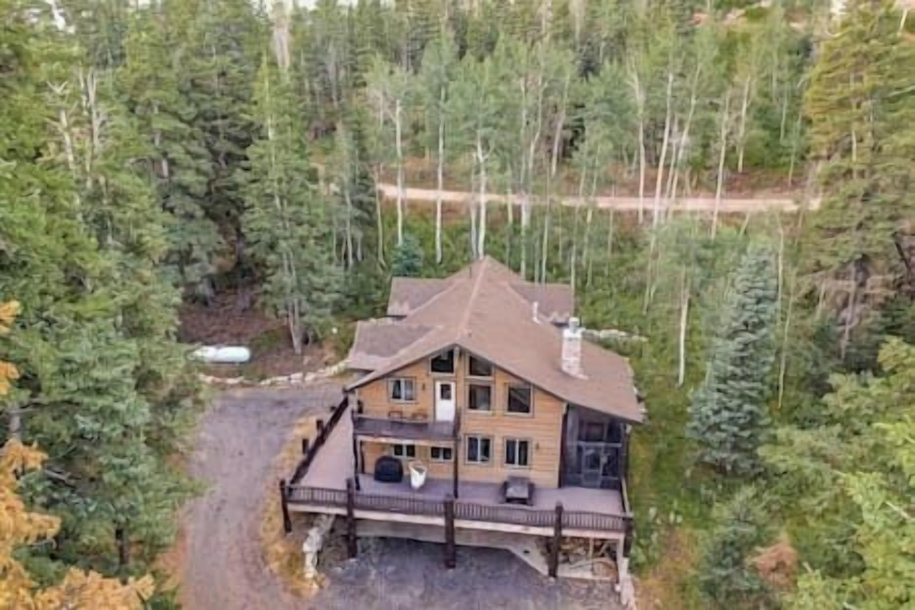 Une cabane en rondins à deux étages, dotée d’une véranda qui fait le tour de la maison, et entourée d’une forêt dense.