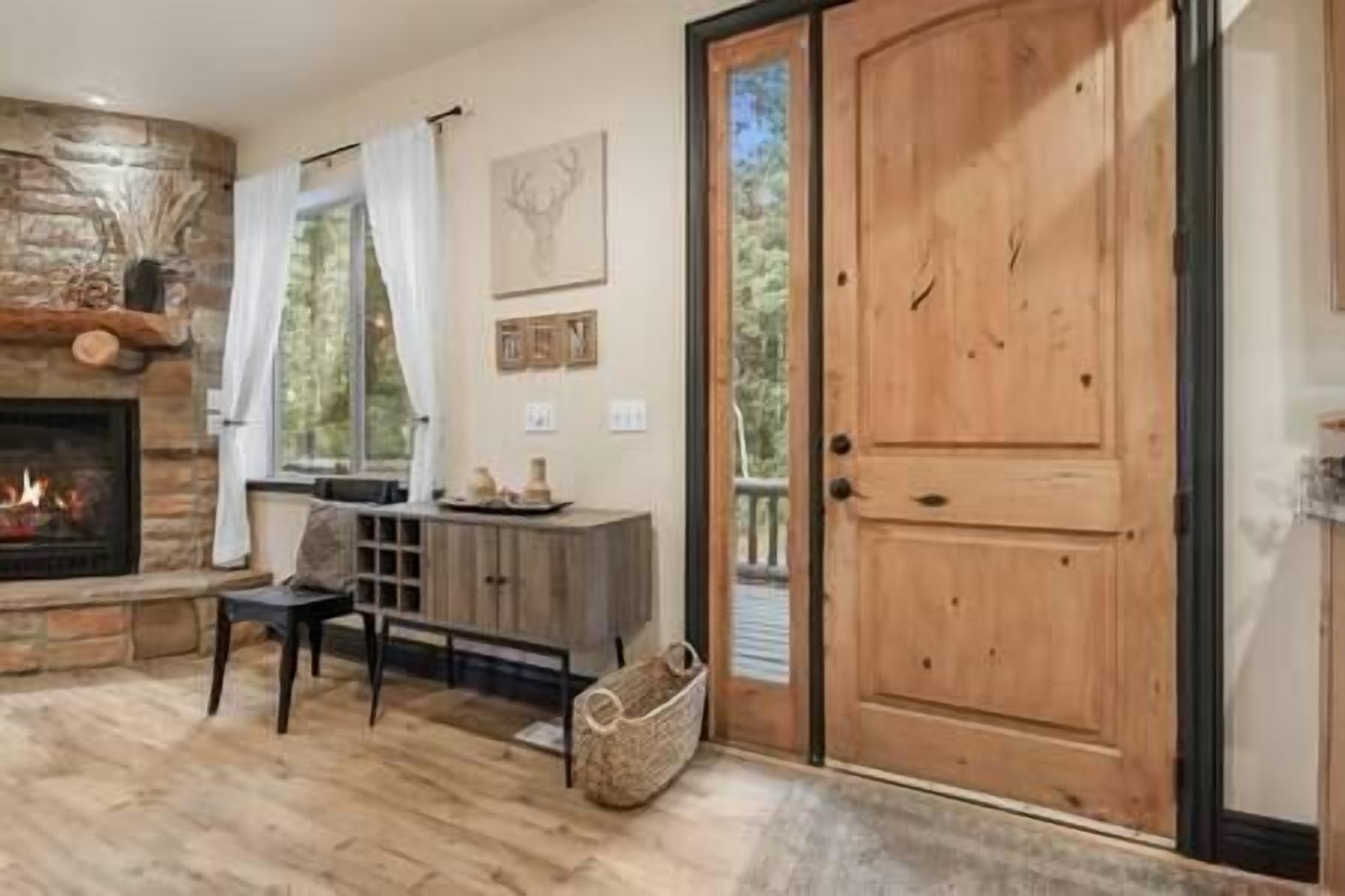 A cozy living room with a stone fireplace, a wooden door, and a view of the outdoors.