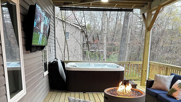 En inglasad veranda med ett bubbelbad, en tv som är monterad på väggen och en soffa i rotting med kuddar.