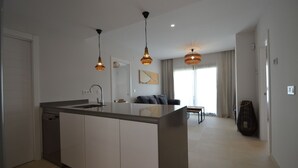 A modern kitchen with a central island, pendant lighting, and a view to a living area with a sofa and curtains.