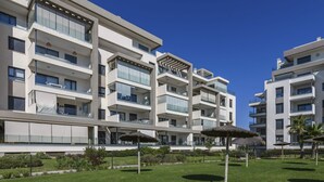 A modern multi-story hotel with balconies, a well-maintained lawn, and outdoor umbrellas.