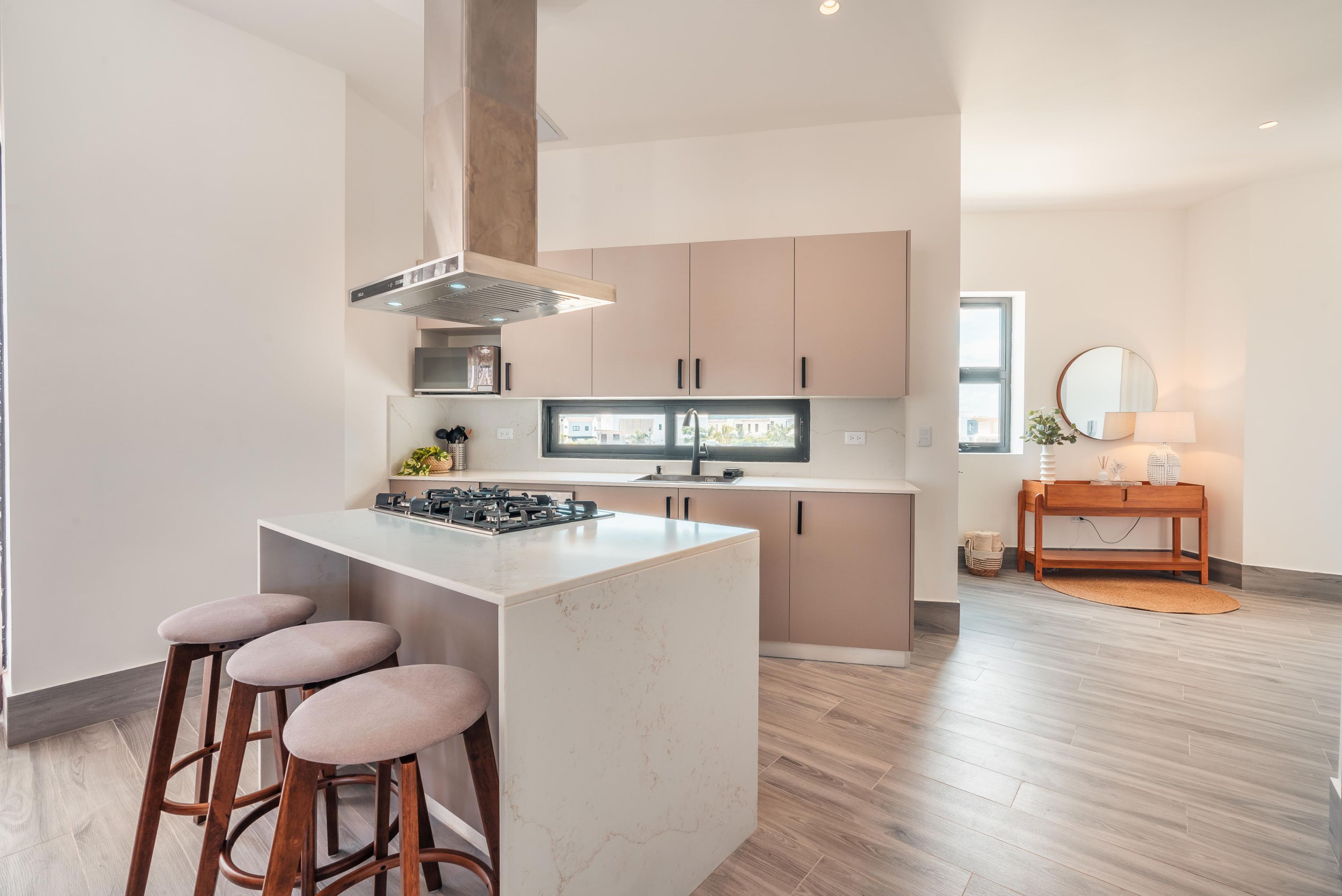 A modern kitchen with a central island, bar stools, and a view of the city through the window.