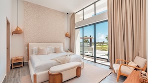 A modern bedroom with a large bed, a bench, a wooden side table, and a view of the outdoors. - Vista Alta 208 in Punta Cana (Punta Cana)