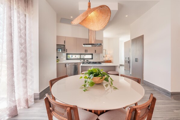 A modern kitchen with a round dining table, wooden chairs, and a hanging light fixture. - Vista Alta 208 in Punta Cana (Punta Cana)