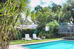 Una piscina con zona delimitada por una valla, rodeada de abundante vegetación y un cartel con las normas de la piscina.